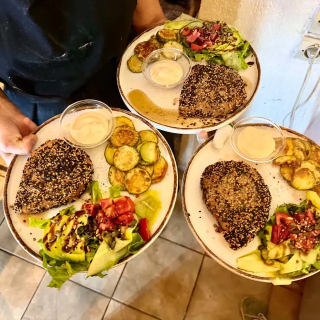 Three plates of sesame-crusted tuna steak with salad